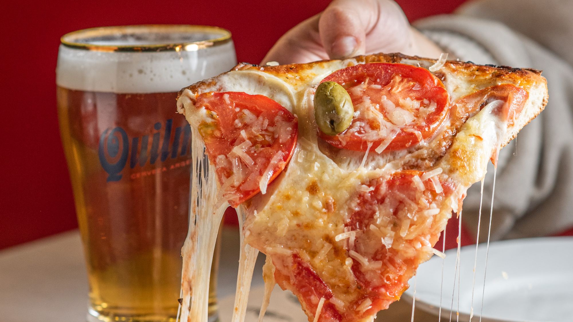 Porción de pizza con queso hilando y un chopp de cerveza